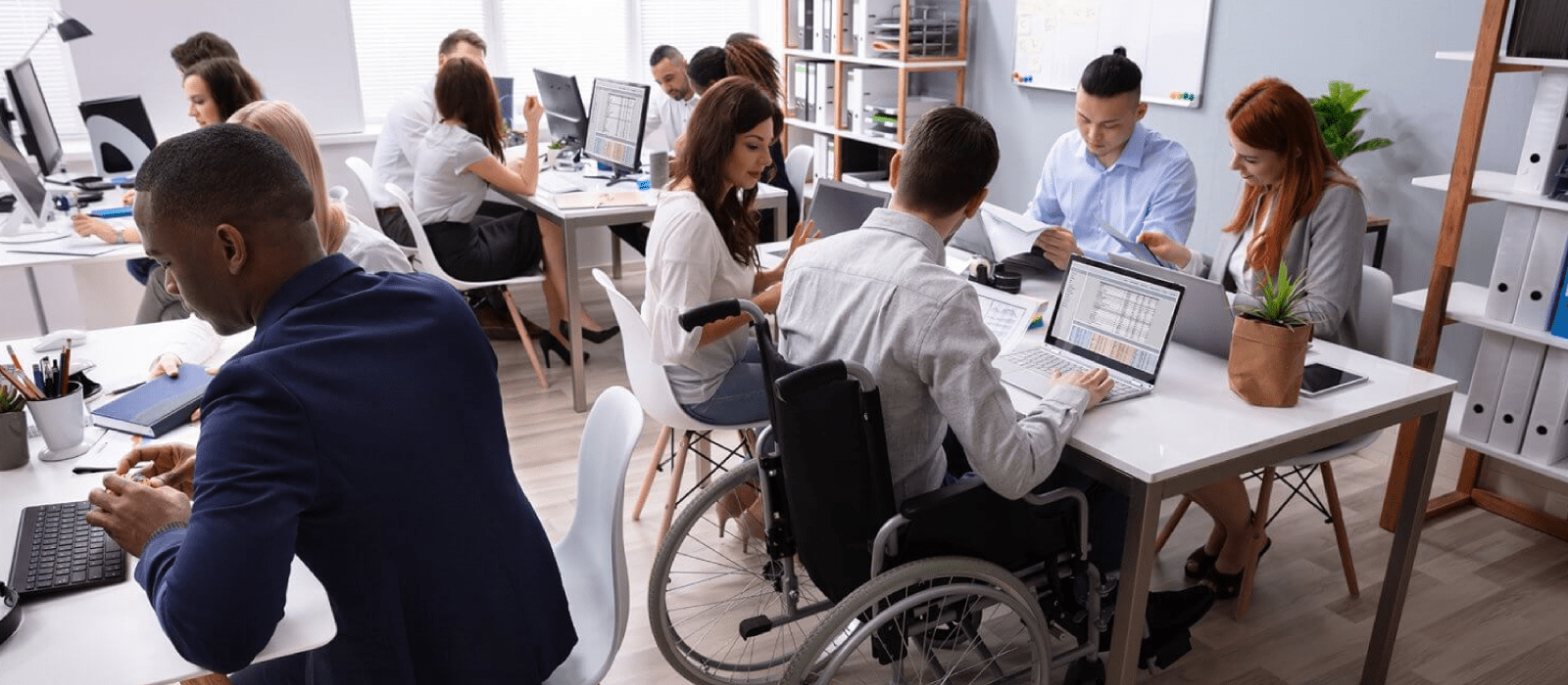 Co-workers around a table in front of their computers working together. One of the people around the table is in a wheelchair.