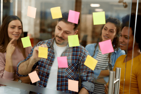 Group of work colleagues doing a brainstorming exercise with sticky notes around a glass board.