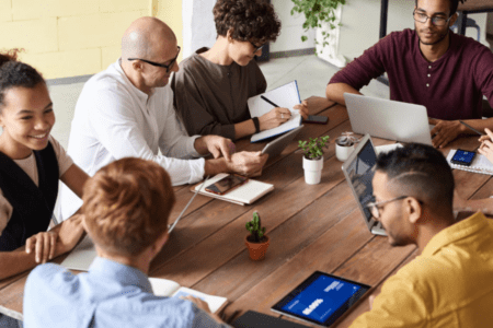 Diverse group of employees around a table with various devices collaborating on a project.