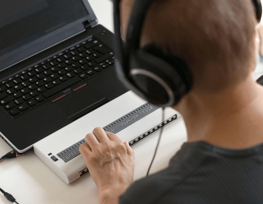 Over the shoulder view of a person with headphones using a braille keyboard on a computer.