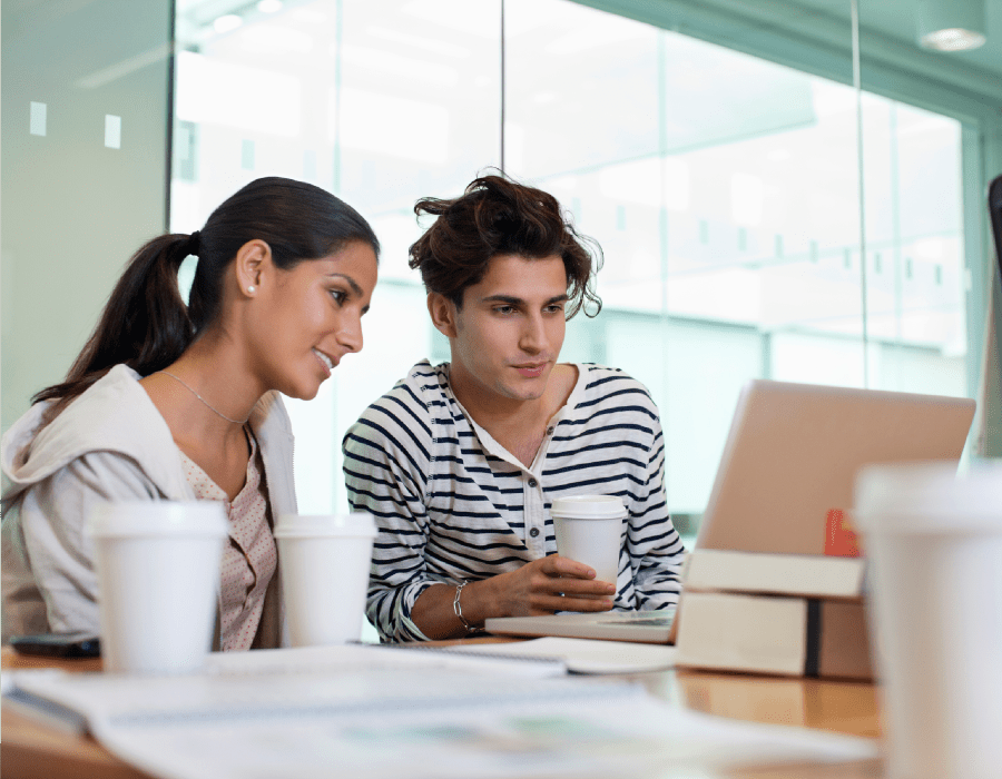 Man and woman reviewing content on a computer while sitting at a conference table in an office environment.