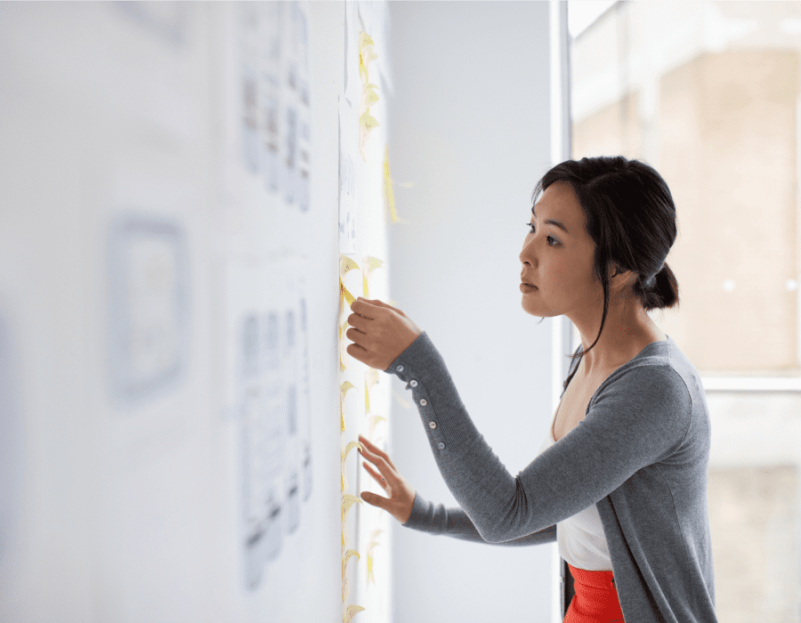 Young woman performing a card sorting exercise on a whiteboard in a work office with large windows.