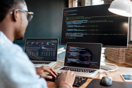 Programmer writing program code in office with three monitors.