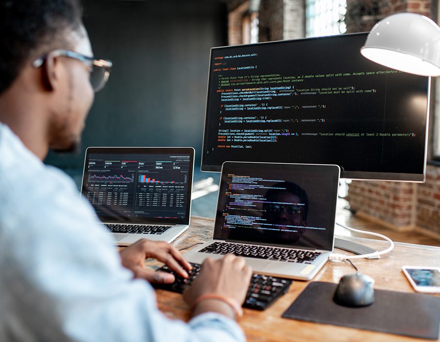 Programmer writing program code in office with three monitors.