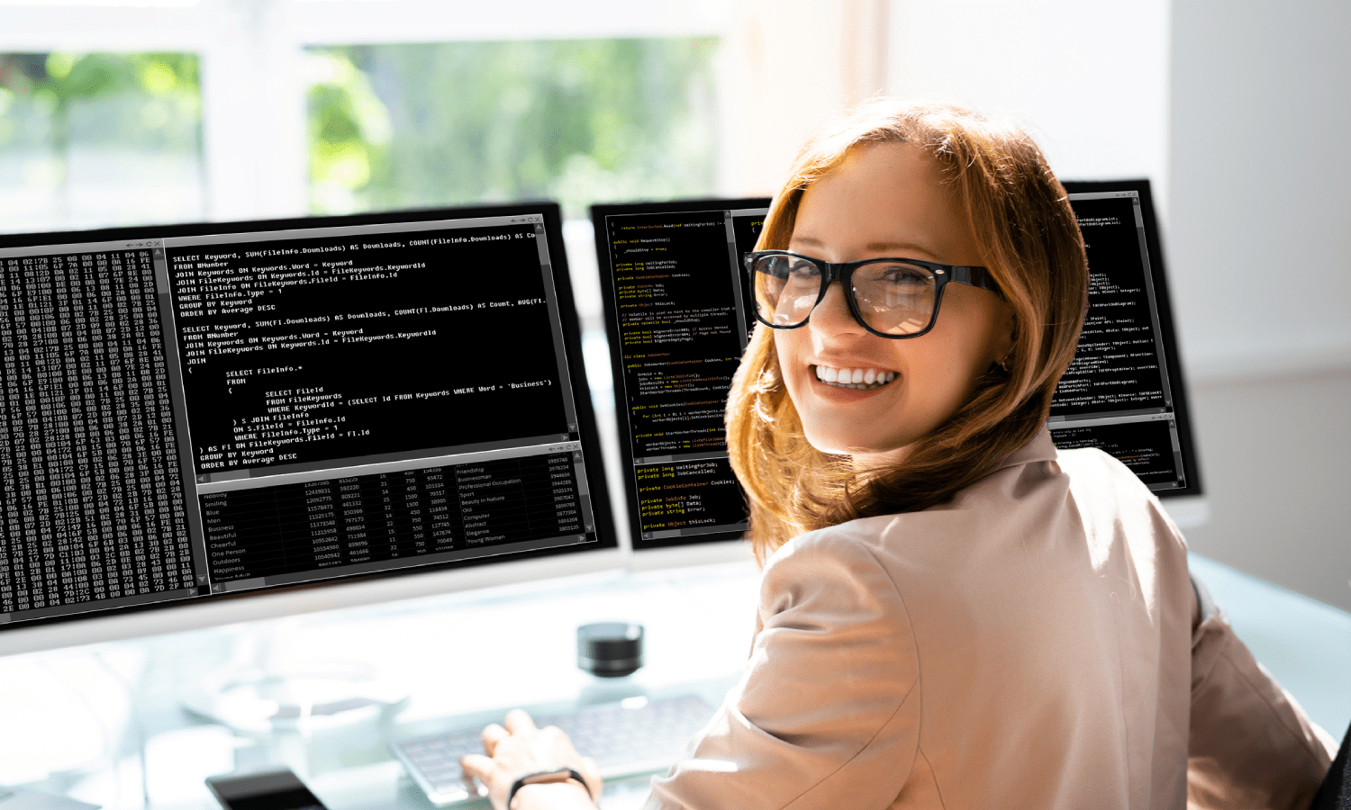 Woman at dual monitors writing code and looking back over her shoulder smiling.