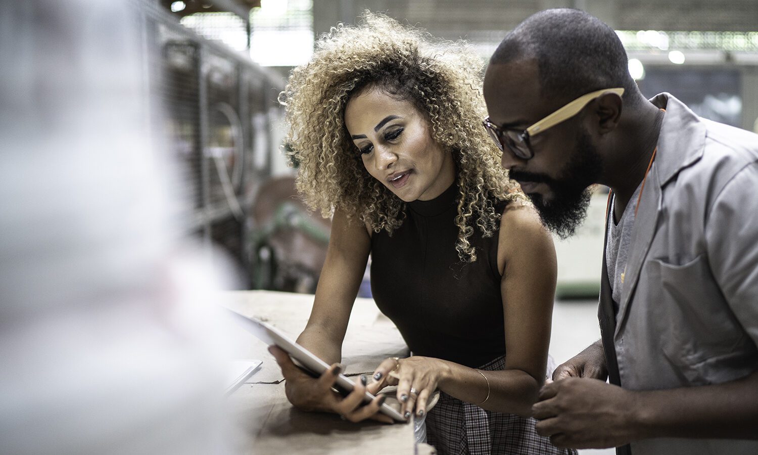 Two coworkers, a man and woman, reviewing data on a tablet in a data warehouse facility.