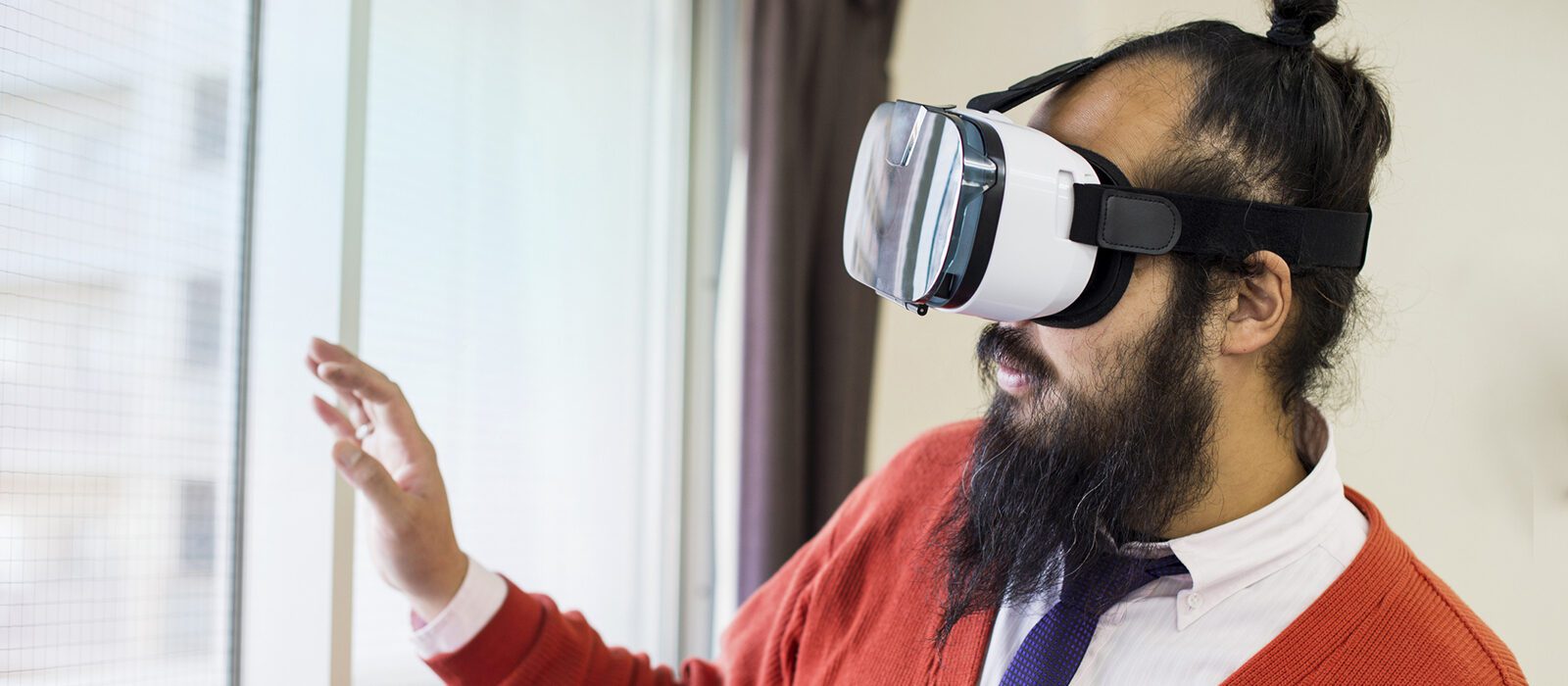 Person wearing virtual reality headset with hands gesturing at something viewing.