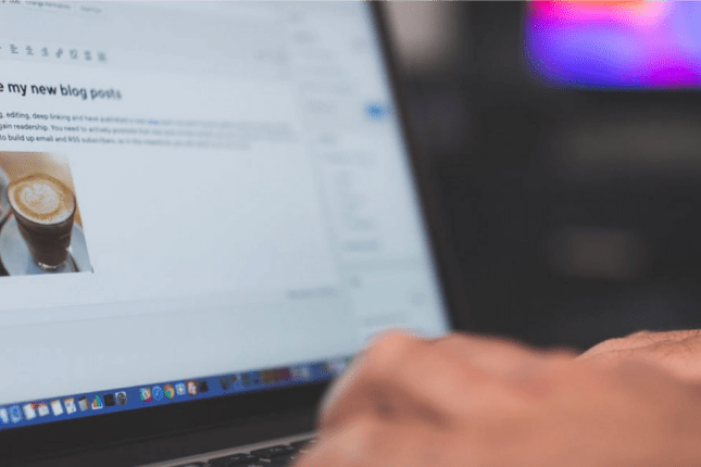 Very closeup shot of hands typing on a laptop with a somewhat blurred view of a blog entry on the screen.