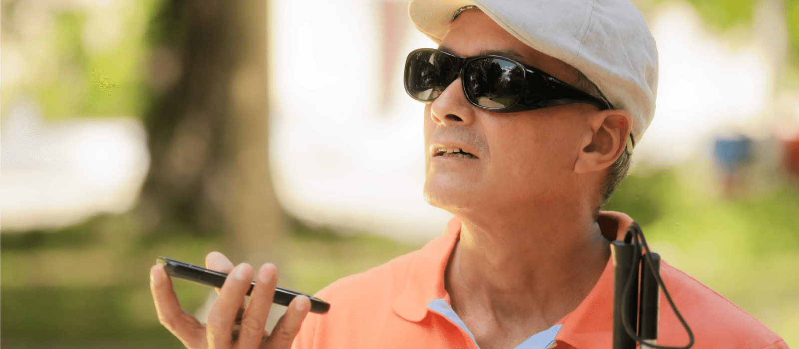 Man wearing dark glasses holding a blind guide cane while speaking on his mobile device.