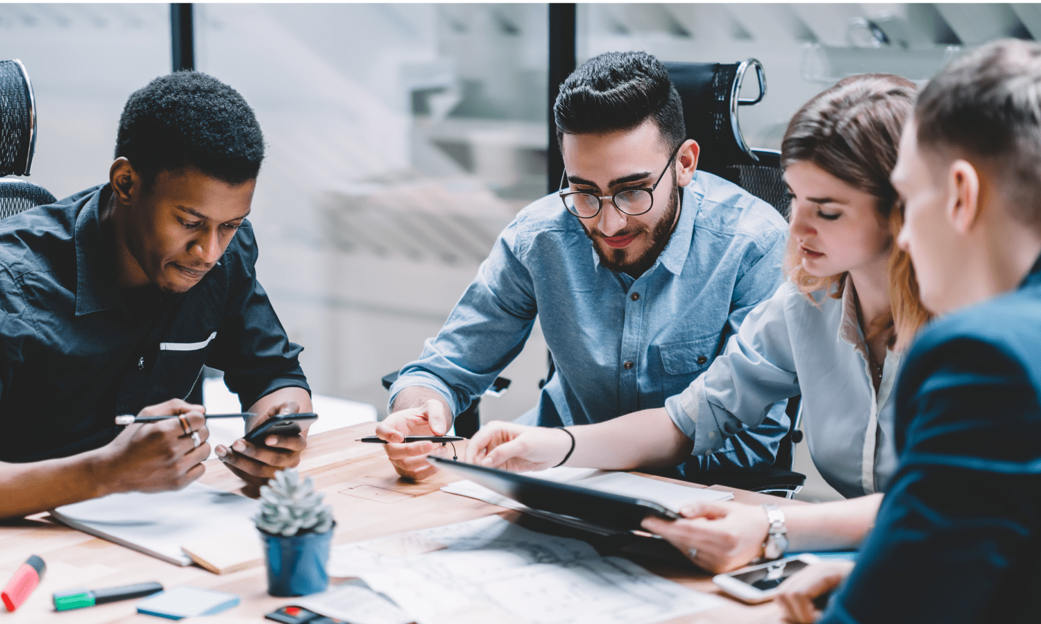 Co-workers around a table in a war room setting reviewing designs on multiple devices.