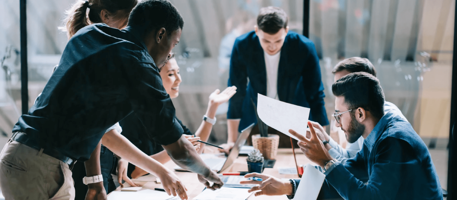 Large group of co-workers around a conference table reviewing both online and hard copy reports.