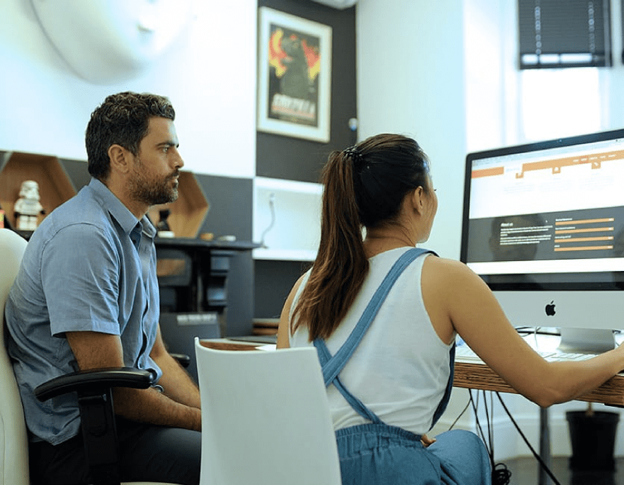 Woman sitting at a desk reviewing a website while a man observes her interactions with the site.