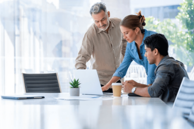 Three colleagues at a table reviewing information on a laptop.
