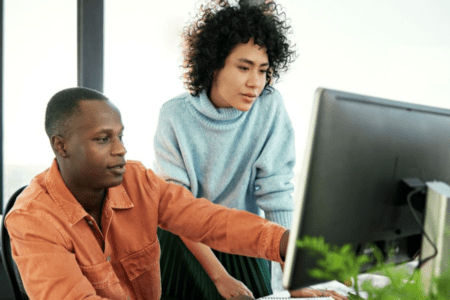 Two colleagues at a computer reviewing information on a screen.