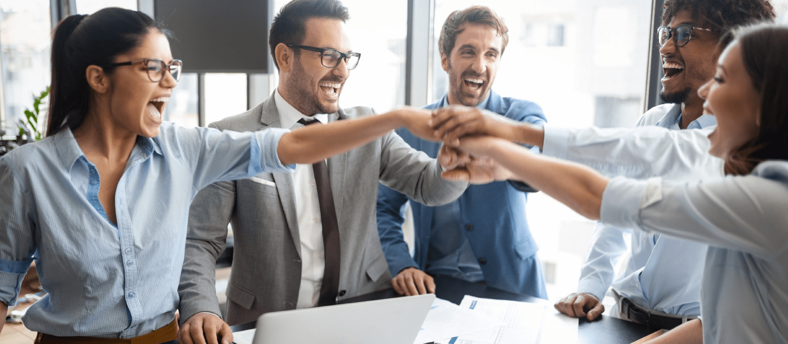 Diverse members of a work team members standing around a raised conference table celebrating an achievement in the workplace.