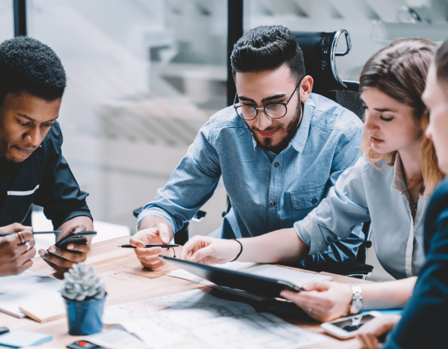 Co-workers around a table in a war room setting reviewing designs on multiple devices.