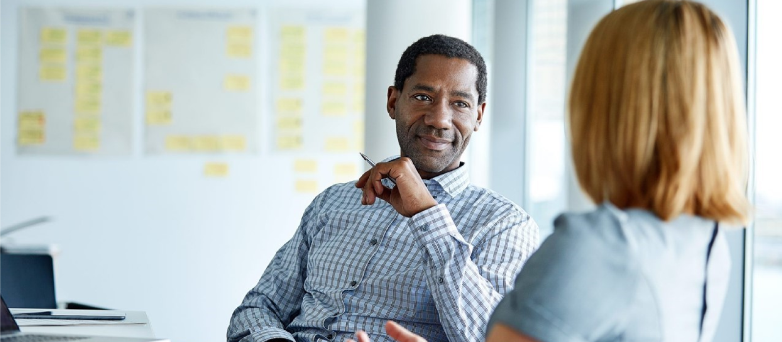 Man and woman meeting in a bright and modern office. Whiteboard with writing and sticky notes is behind them.