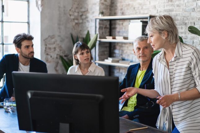 Group of coworkers discussing a project around a computer screen at an office desk.