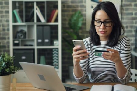 Portrait of young woman making payment with credit card using smartphone at work.