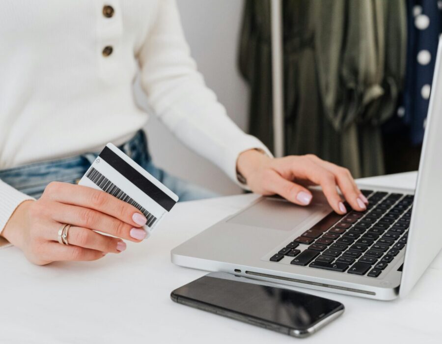 Torso and arms of a woman holding a credit card and typing on a laptop.