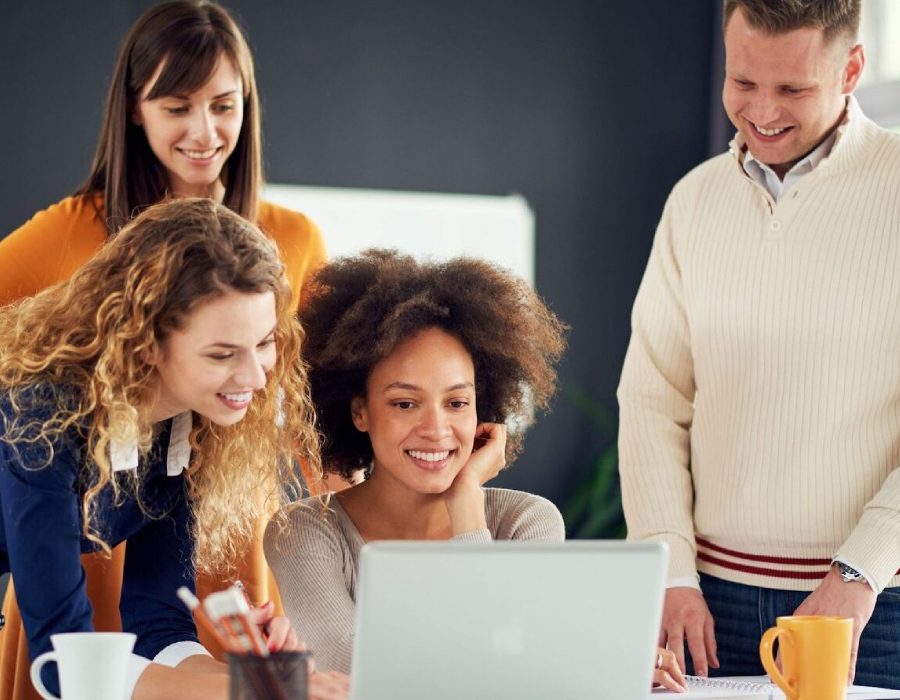 Colleagues gathered around a laptop smiling.
