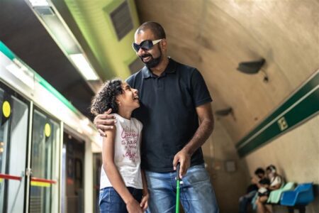 Blind father smiling and talking while walking with his daughter at a subway station.