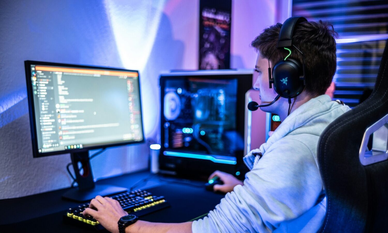 A gamer smiles and concentrates on his screen. He wears a headset with a mic.