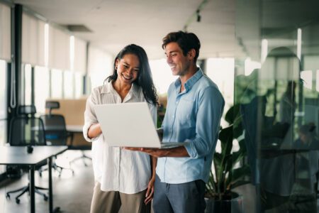 Two business people working talking using tablet tech walking in corporate office. They wear business casual clothes and are smile.
