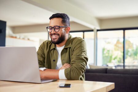 A smiling member of the accounts payable team sits in front of his laptop, with his arms crossed on the desk.