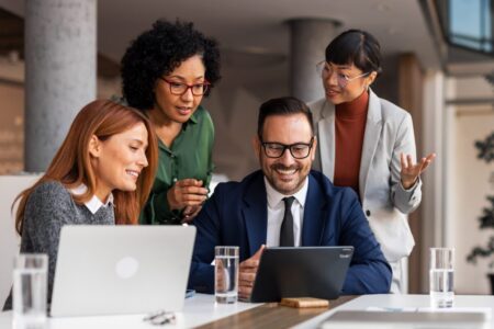 A group of four professionals (three women and one man) engaged in discussion around a laptop.